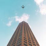 bottom view shot of airplane flying above high rise building